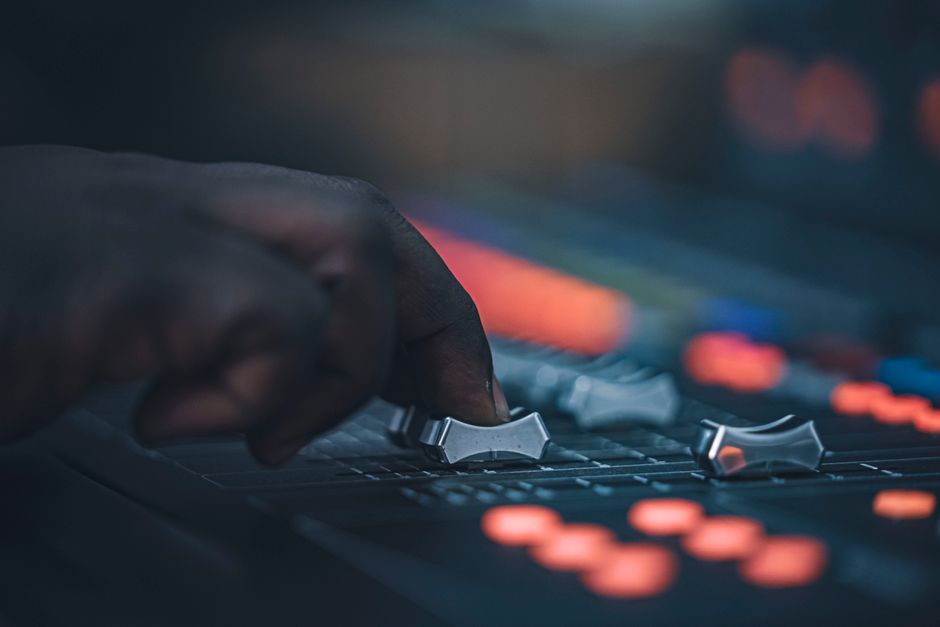 A hand adjusting sliders on a professional audio mixing console in a dimly lit studio setup.