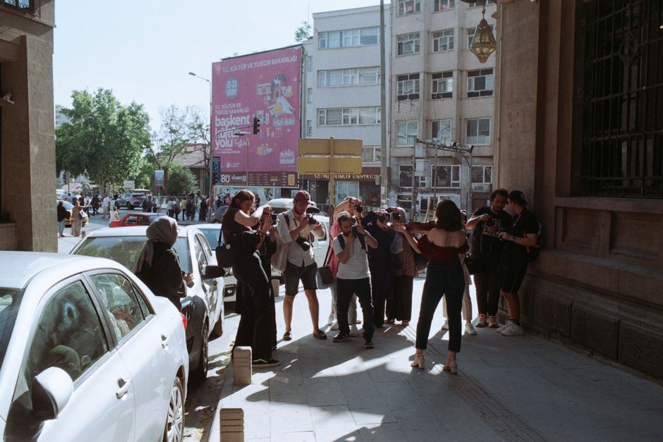 A group of photographers takes photos of a woman posing on a bustling city street, creating an urban photography scene.