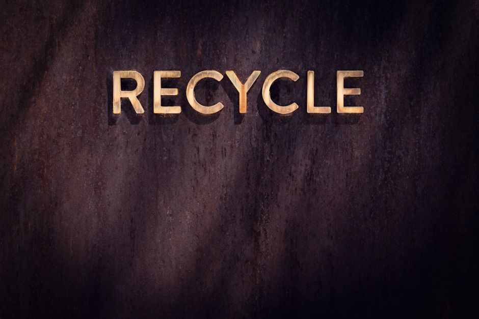 Golden "Recycle" sign on a rustic wood wall, highlighting eco-friendly concepts.