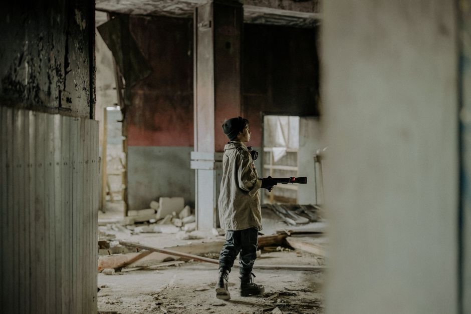 A boy with a flashlight explores a desolate, ruined building, evoking themes of post-apocalypse and survival.