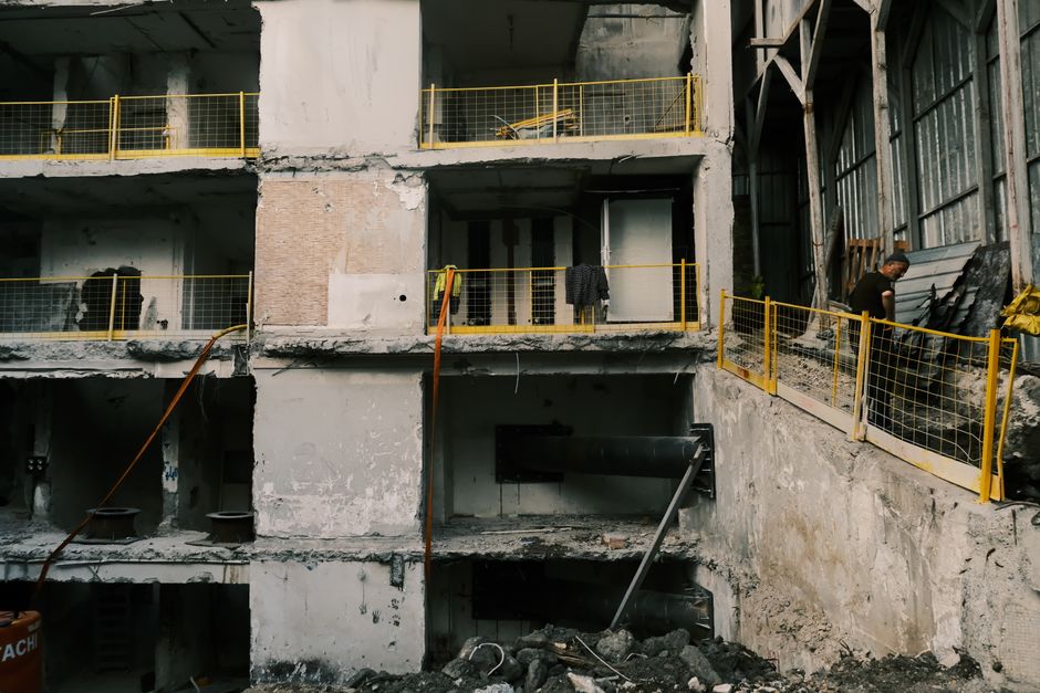 A partially demolished building with exposed interiors and construction worker.