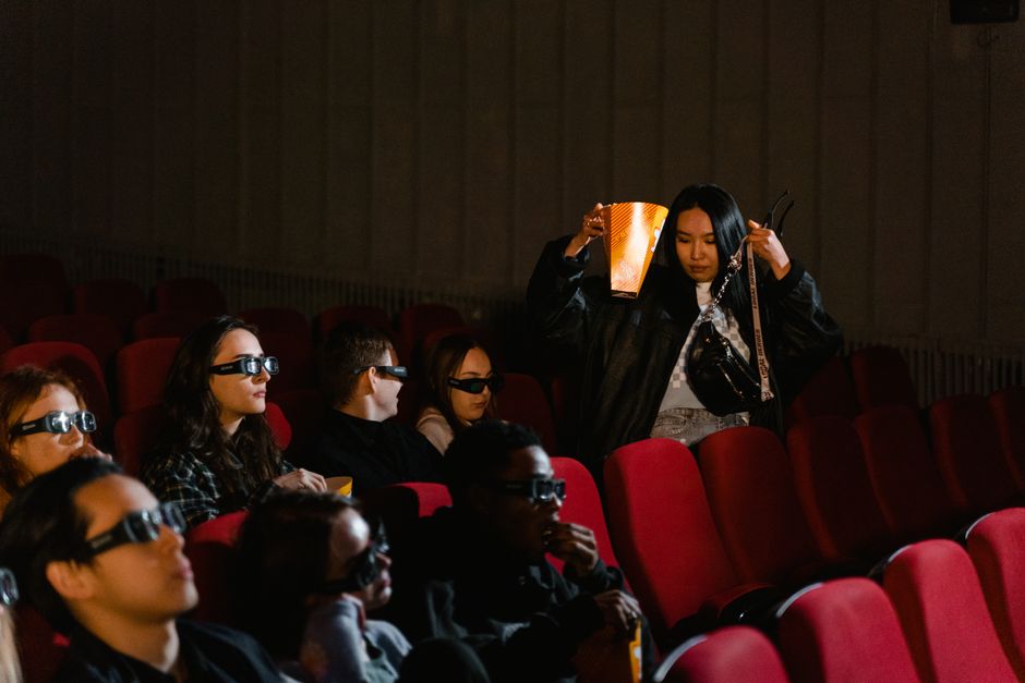 A group of diverse people watching a movie in a theater wearing 3D glasses and eating popcorn.