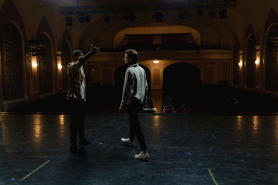 Two men on stage practicing a scene in an empty theater, demonstrating drama and performance art.