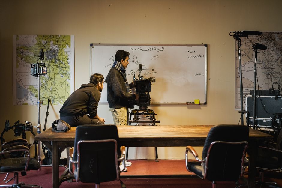 Two men setting up a camera in an indoor film studio. Maps and equipment surround them.