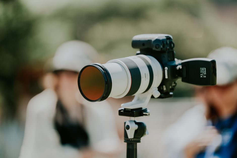 Professional camera with telephoto lens on tripod, blurred outdoor background, showing focus and precision.