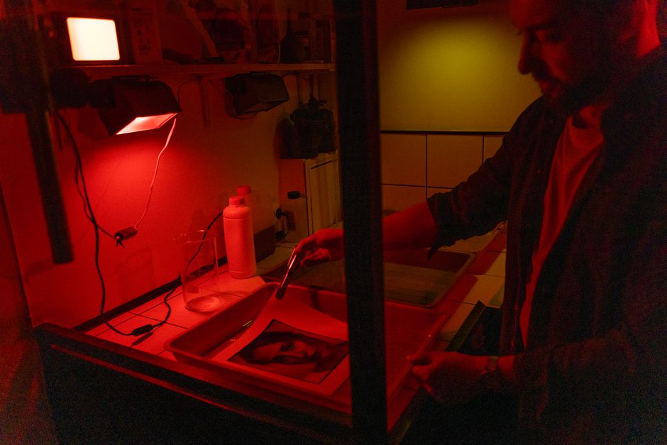 A photographer develops film in a darkroom under red light, showcasing the classic processing method.