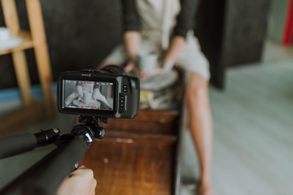 Video camera recording a ceramist shaping clay pottery on a spinning wheel.