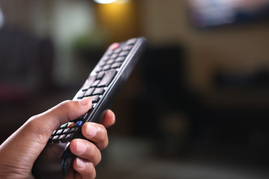 Hand holding a TV remote control, focusing on buttons and grip indoors.