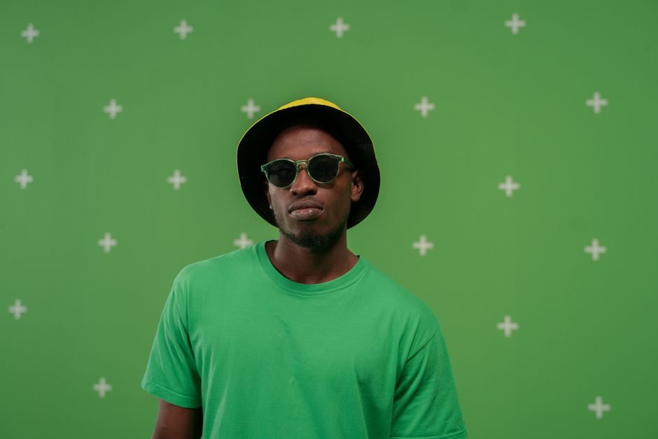 Man wearing green shirt and sunglasses stands against a green screen with visual effects.