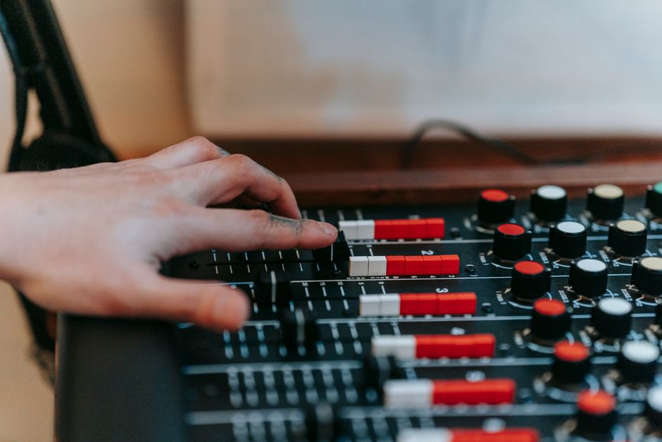 A hand adjusting sliders and knobs on a professional audio mixer in a recording studio.