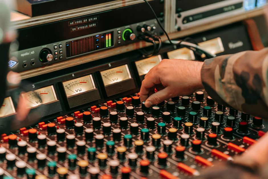 Close-up of a hand adjusting knobs on a professional audio mixing console in a recording studio.