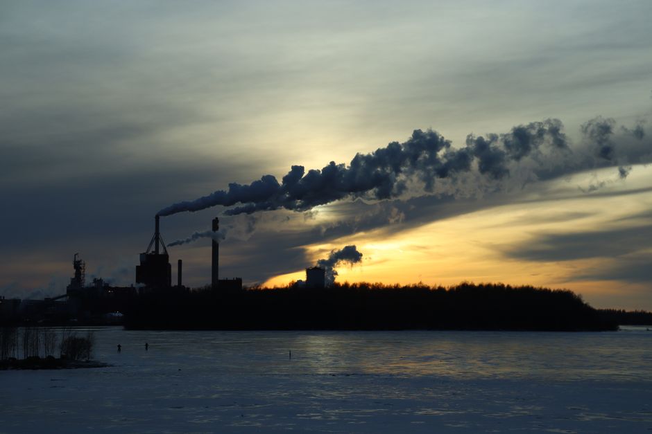 Factory chimneys emit smoke under a cold winter sunset. Pollution is evident.