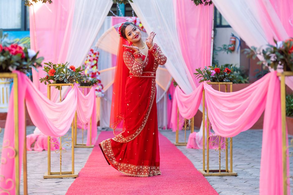 A bride in a stunning red saree poses gracefully at a beautifully decorated wedding venue.