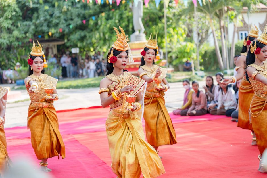 Colorful traditional Cambodian dance performance with women in elegant costumes on red carpet outdoors.