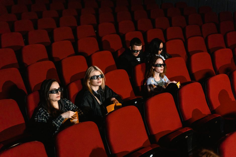 Group of people wearing 3D glasses in a cinema watching a movie, enjoying popcorn.