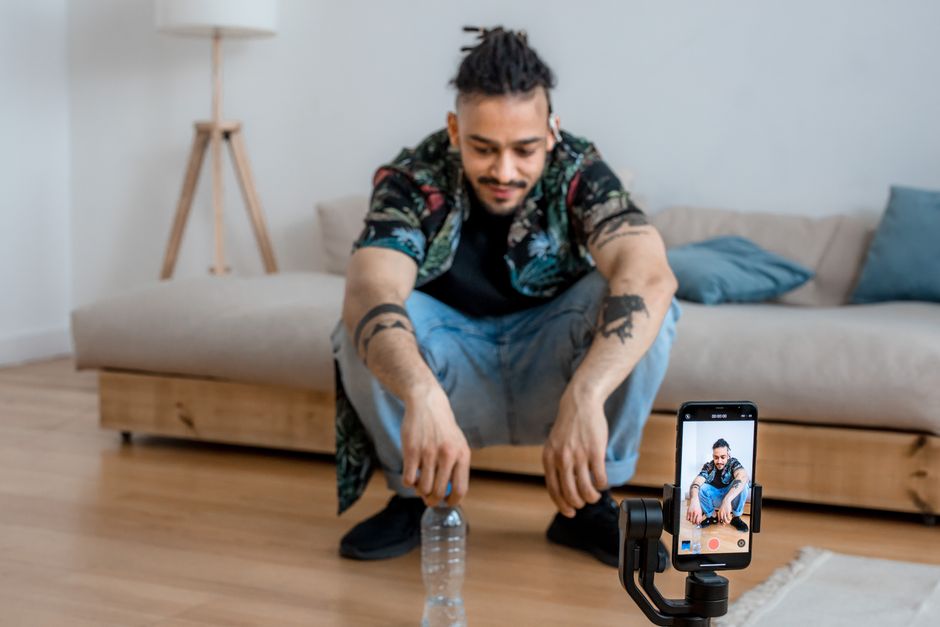 Young man recording content in living room with smartphone on a tripod.