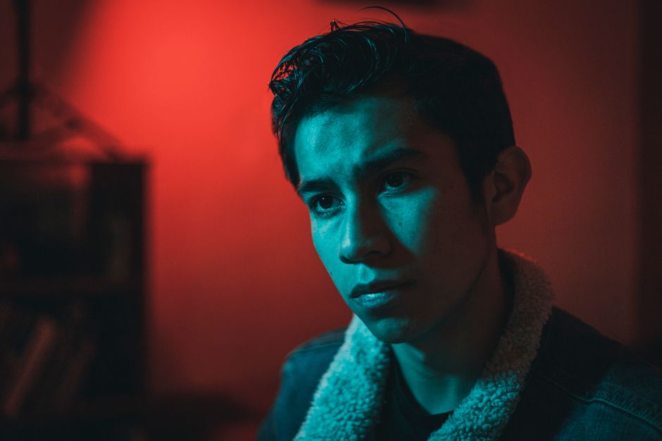 A dramatic portrait of a pensive young man under red and blue lighting.