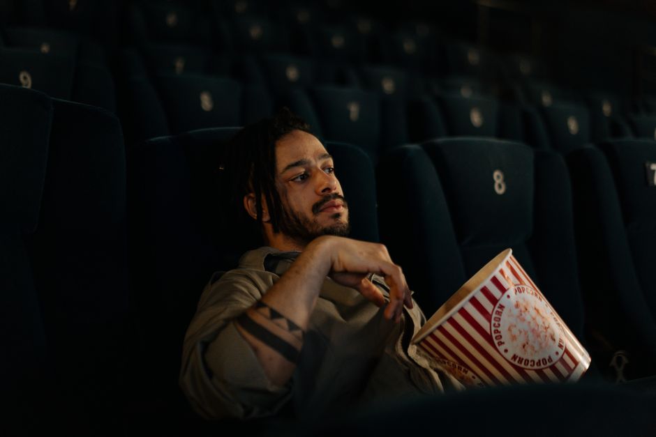 Man sitting alone in a movie theater, holding a large bucket of popcorn.