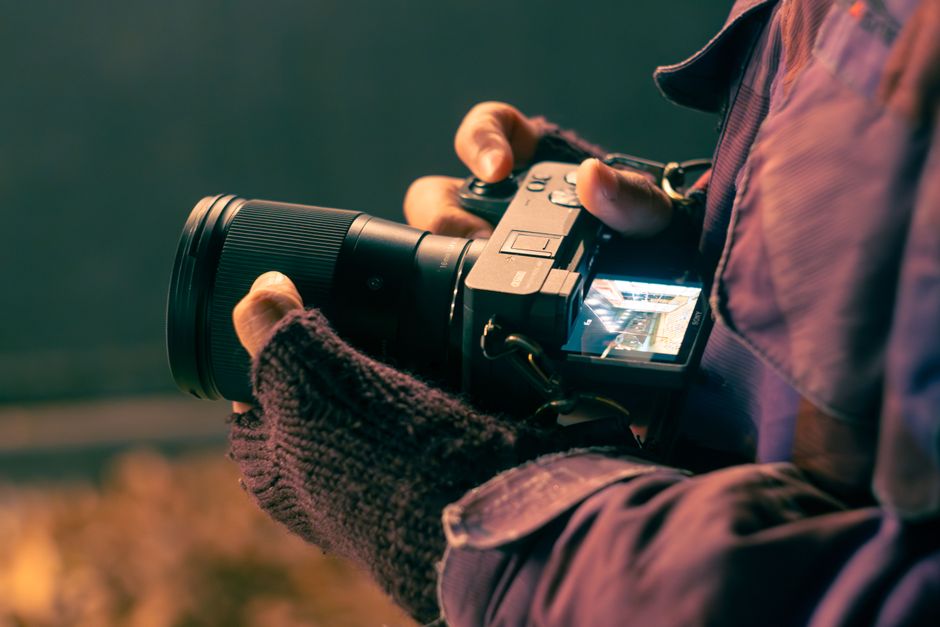 A photographer in gloves adjusts camera settings outdoors in El Bolsón, Argentina.