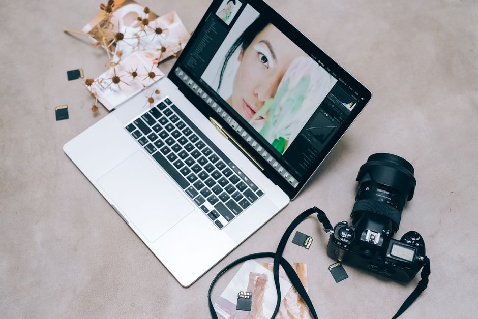 Flat lay of a laptop with photo editing software, camera, and memory cards on a desk.