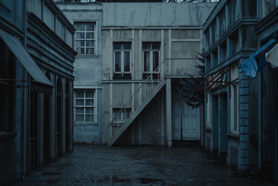 Wet paved sidewalk between shabby residential buildings with canopy against old house with staircase located in neglected district of city