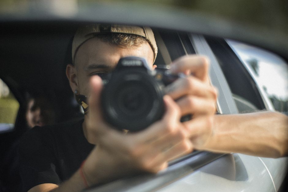 Photographer capturing reflection via car mirror. Natural light, candid moment.