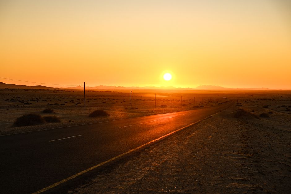 A scenic view of a deserted road against a striking orange sunset in the desert.