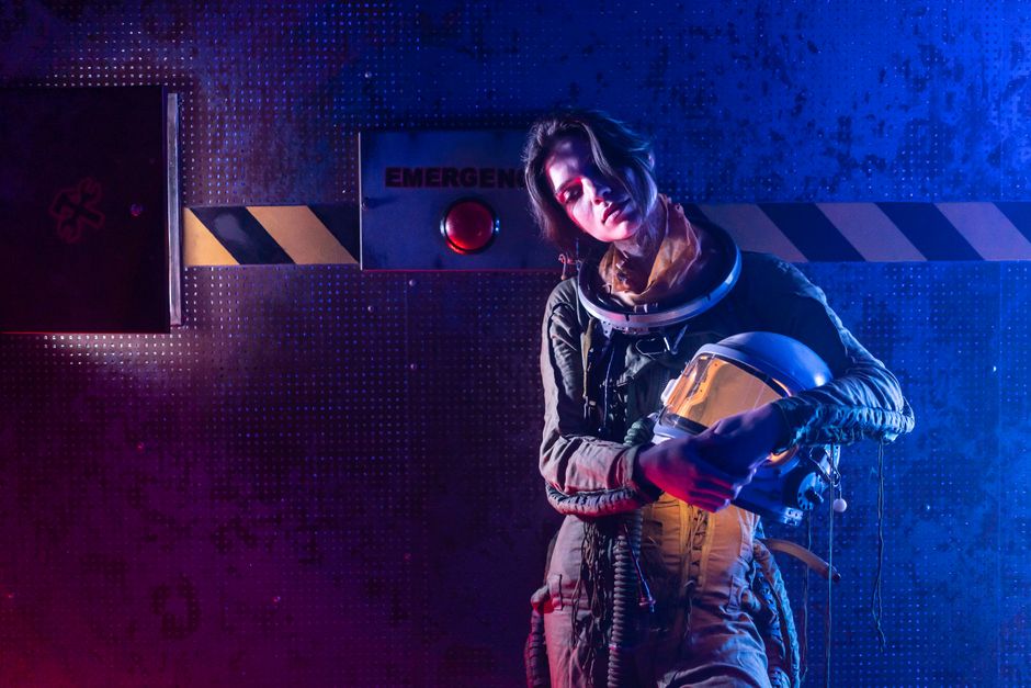 Portrait of a woman in a space suit in a dark, futuristic setting with dramatic lighting.