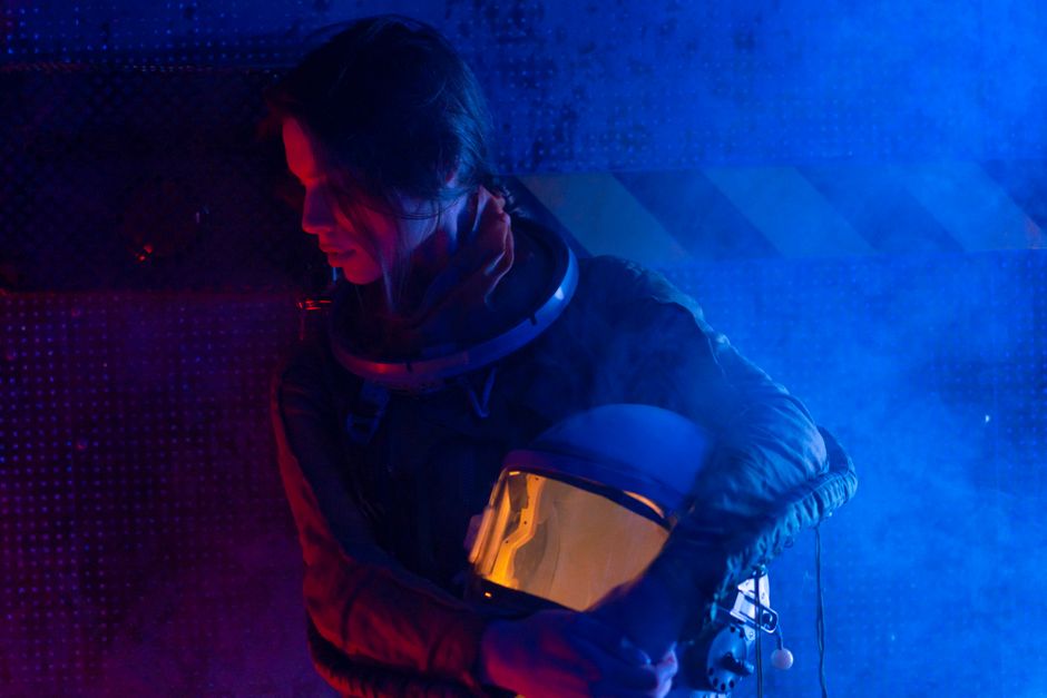 A futuristic portrait of a female astronaut holding her helmet in a dramatic blue light setting.