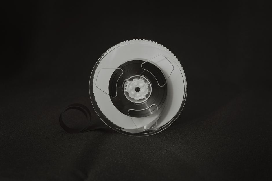 Monochrome image of a vintage reel-to-reel audio tape spool on dark background.