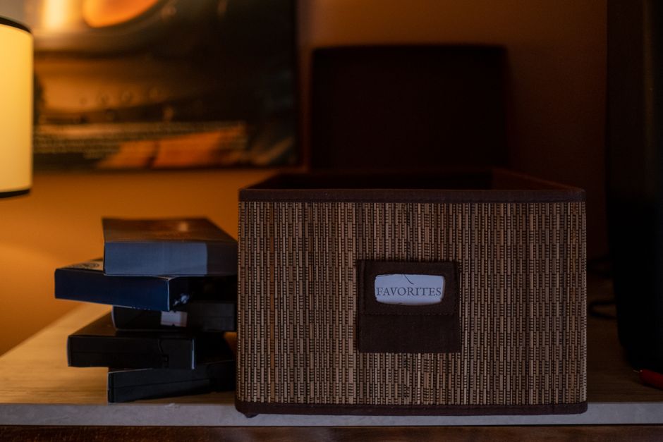 A collection of vintage VHS tapes stacked next to a woven storage box labeled 'Favorites' in a cozy indoor setting.