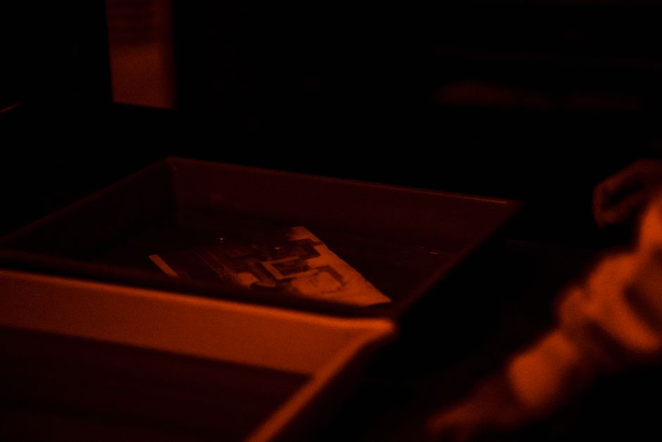 Moody scene of photo developing in a darkroom under red light ambiance.