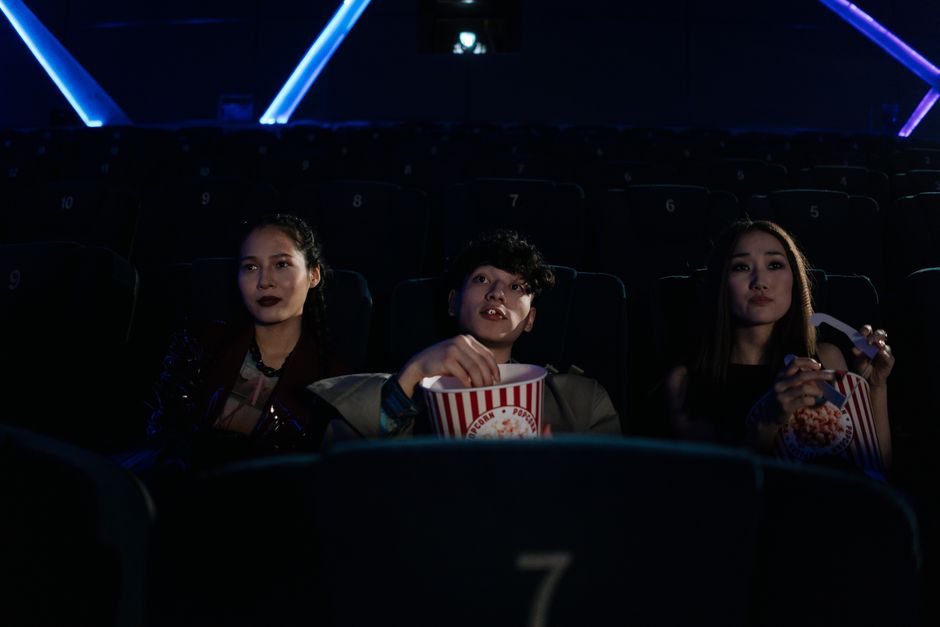 Three friends watching a movie in a theater, enjoying popcorn together.