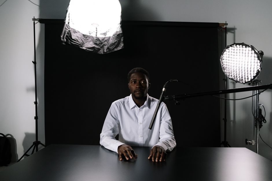 Man in a podcast studio sitting at a table with microphone and lighting equipment.