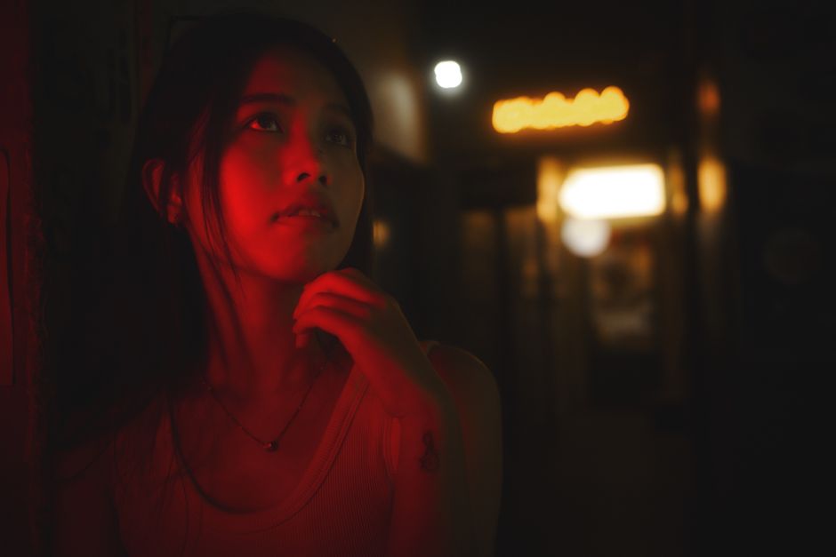 Mysterious woman in an ambient red-lit hallway at night, evoking a contemplative mood.
