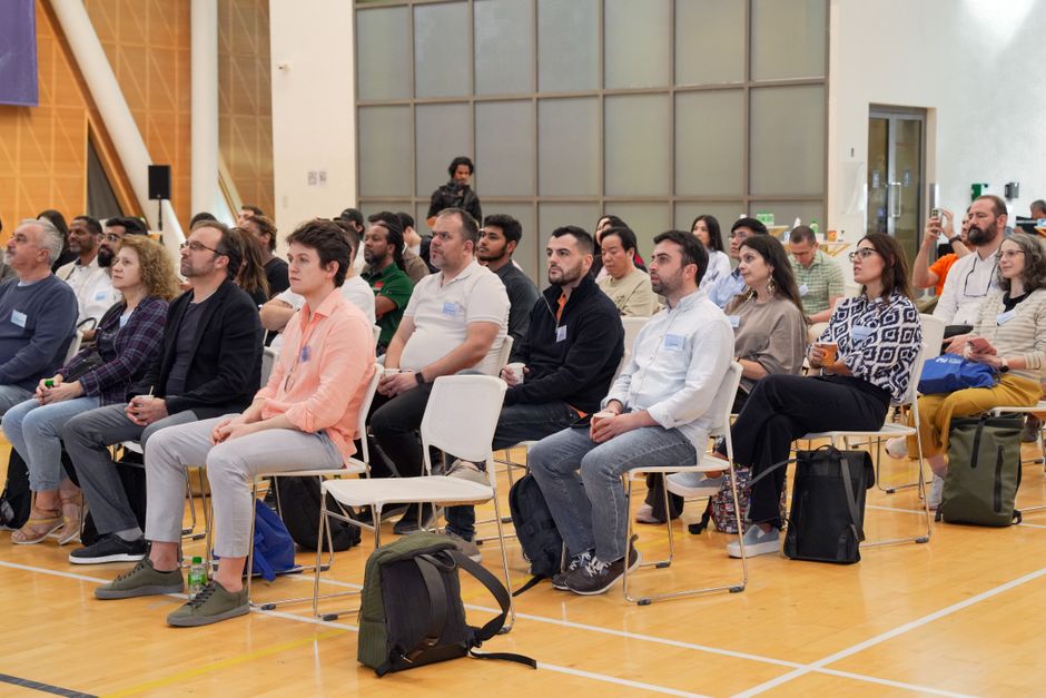 A diverse group of adults attentively listens in an indoor conference setting.