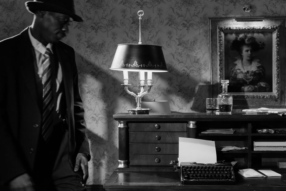 Moody black and white photo of a detective in a vintage office, evoking classic noir cinema.
