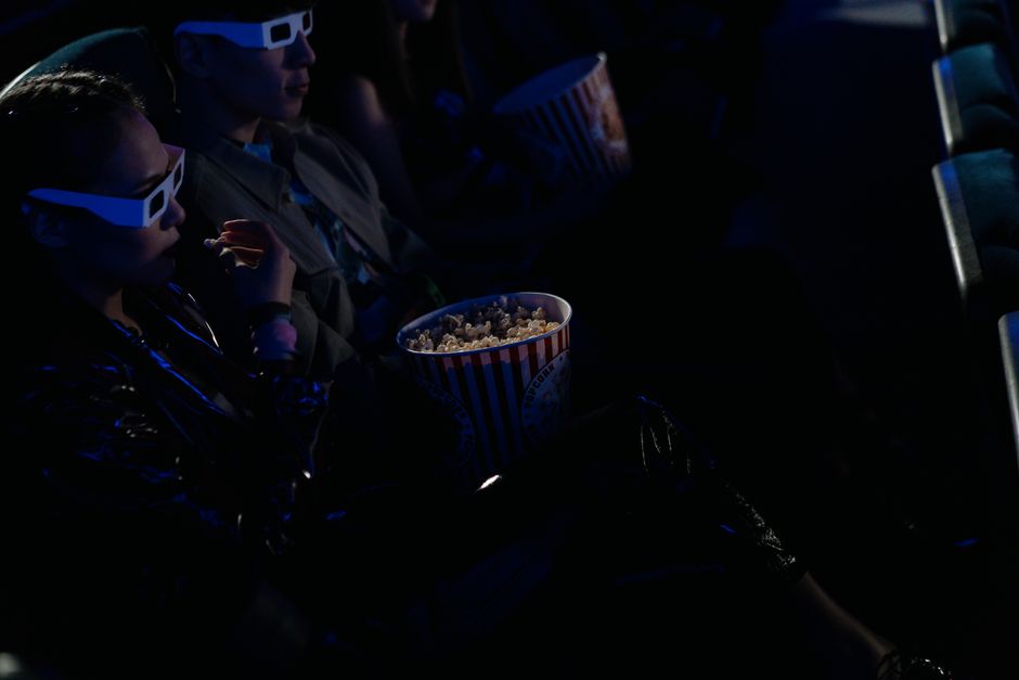 Audience at a cinema enjoying popcorn while watching a movie in 3D glasses.