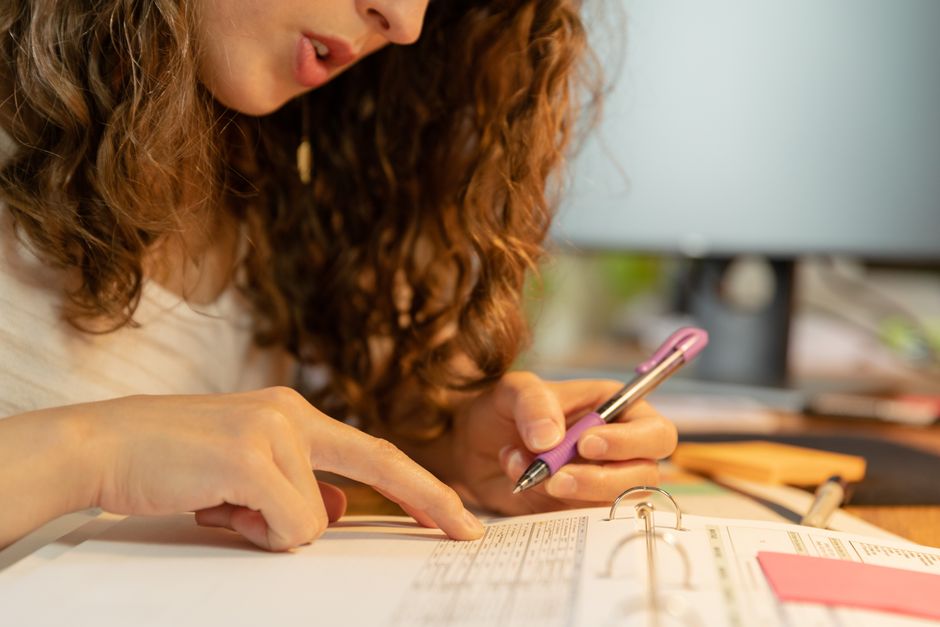 Focused woman pointing and writing on paper in binder with a purple pen.