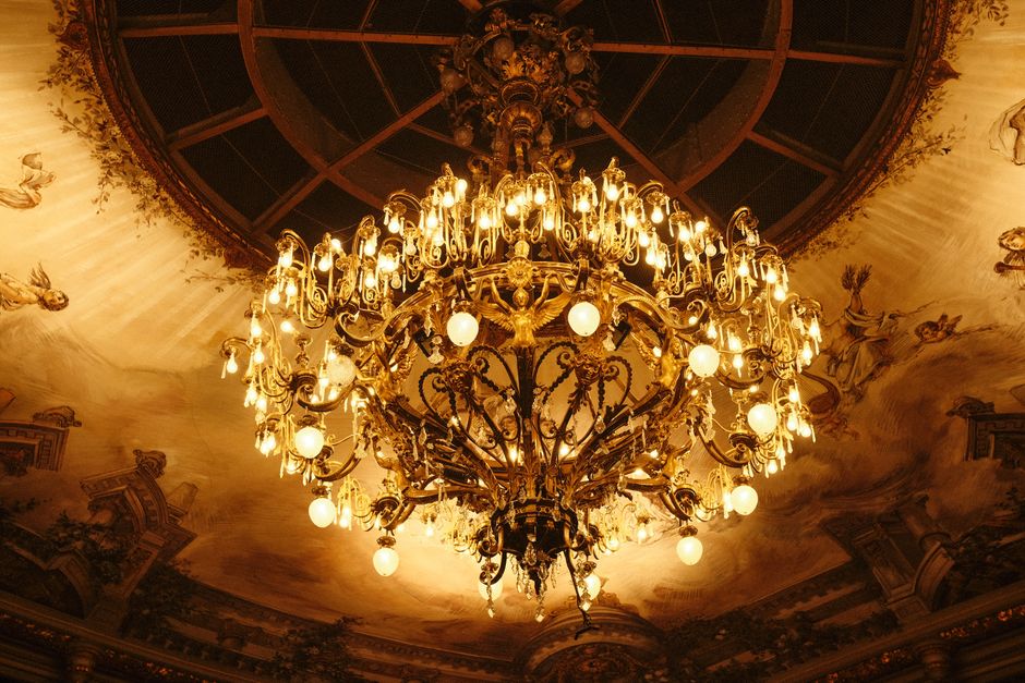 Opulent chandelier in grand ballroom with baroque architecture and decorative ceiling.