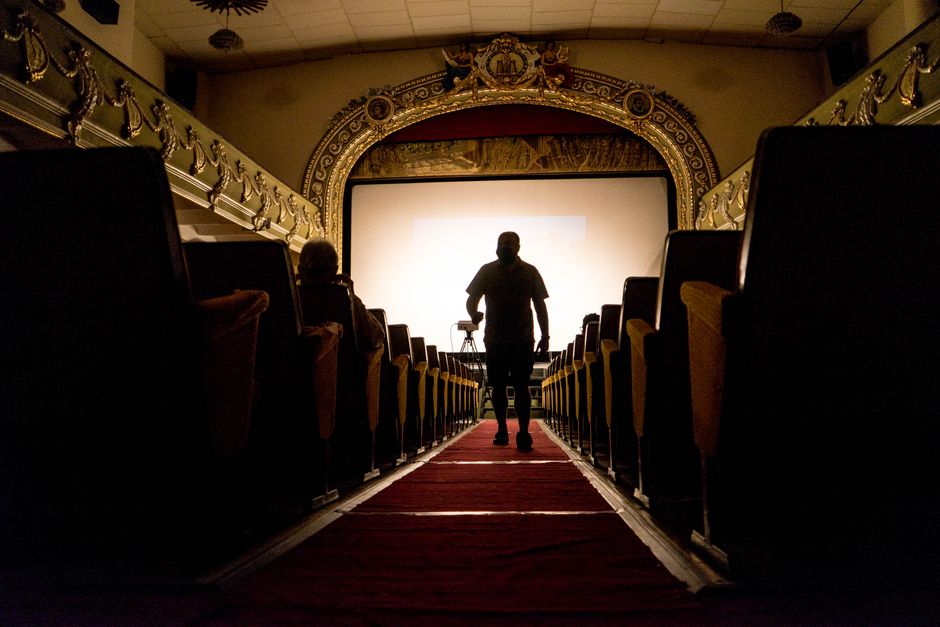 A person walking down an aisle in a vintage theater, showcasing ornate decor.