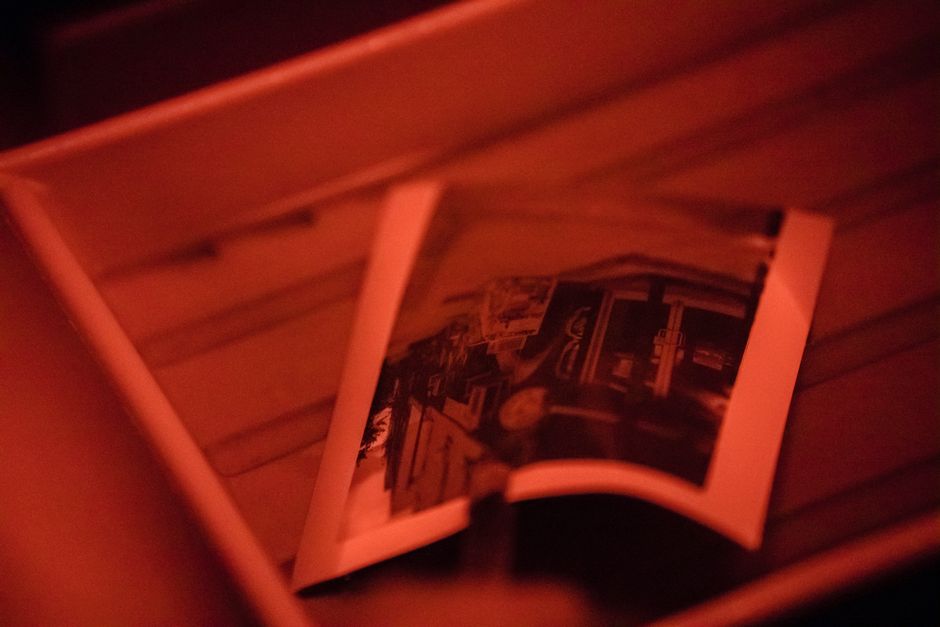 A traditional analog photograph being developed in a darkroom under red lighting, showing the classic process.