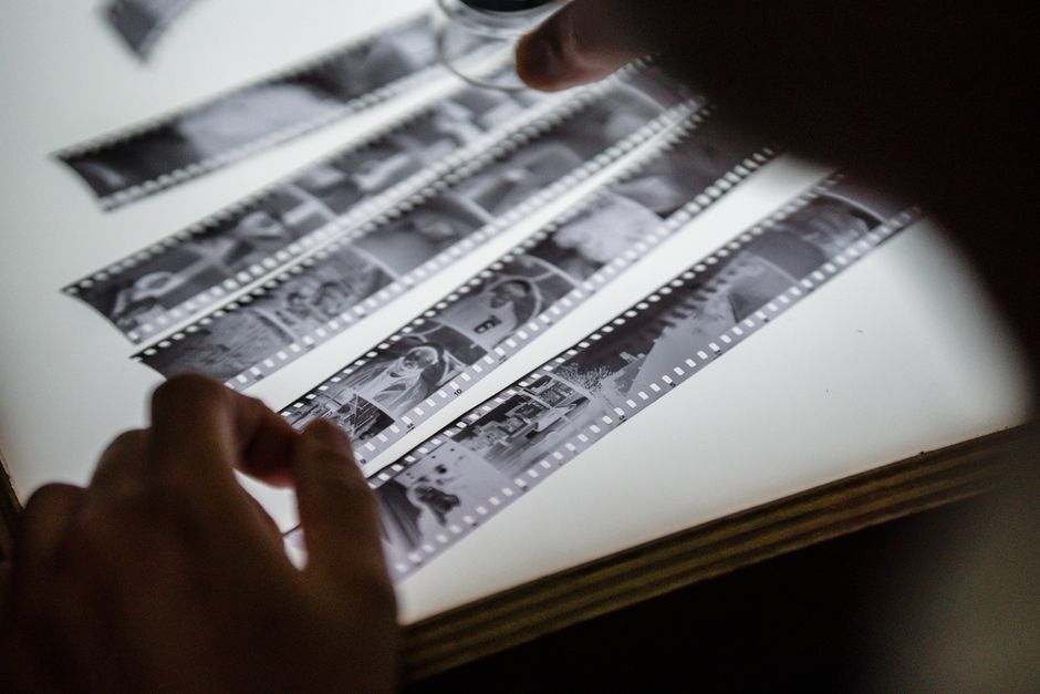 Close-up of hands examining vintage film strips on a light table, evoking nostalgia.
