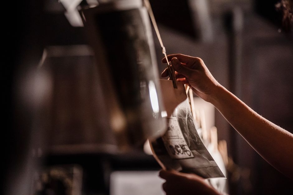A detailed view of hands hanging photographs for development in a dimly lit darkroom.