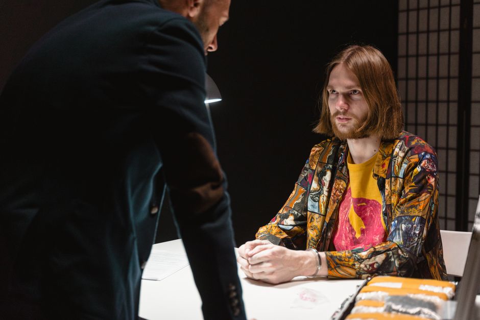 Tense interrogation scene with two men in a dimly lit room filled with suspense.