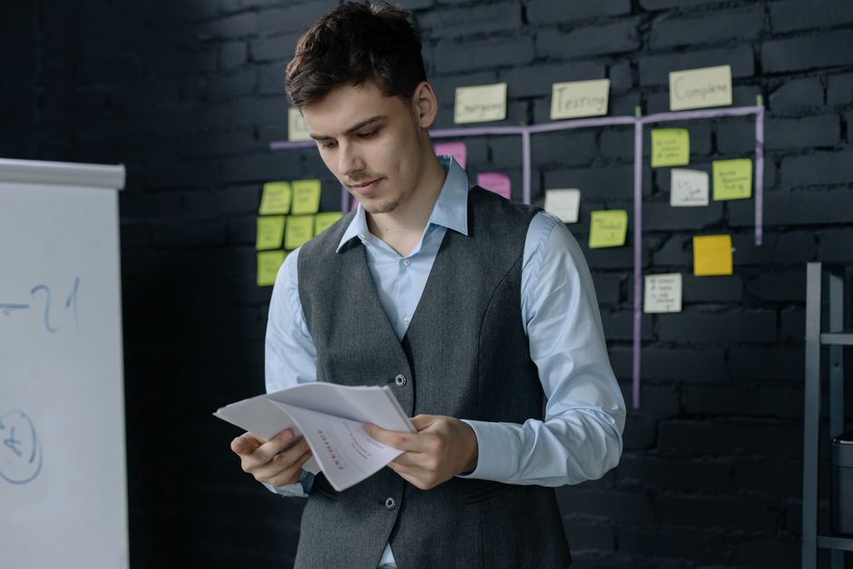 A young man reviewing documents in an office with a black brick wall and sticky notes background.