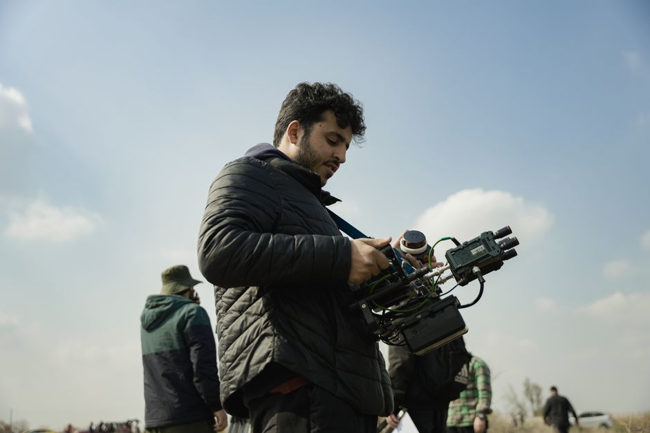 Videographer sets up camera rig outdoors with clear sky and casual attire, capturing scenic shots.