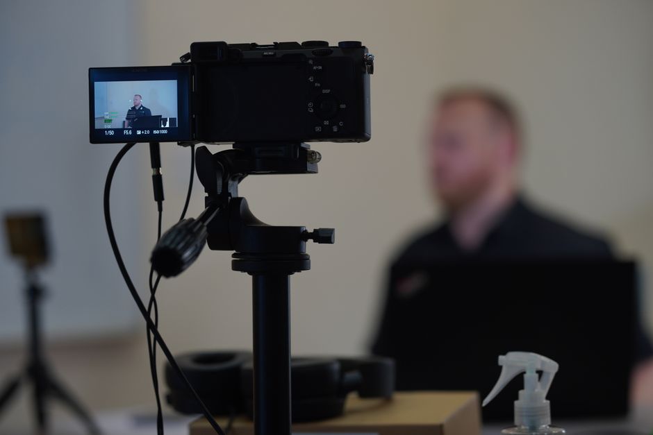 Close-up of camera setup during an indoor filming session with a blurred speaker in the background.