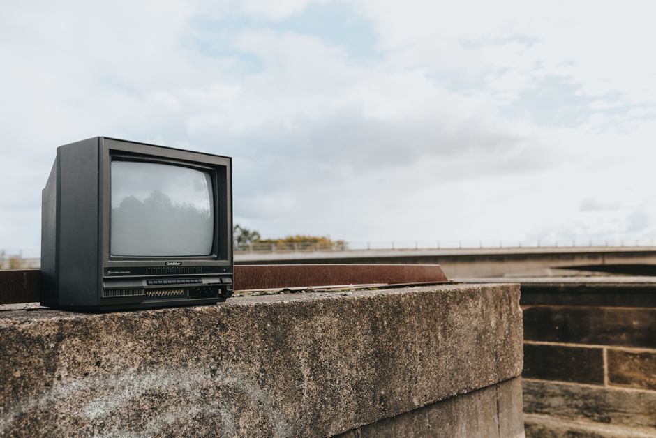 Small old fashioned black television placed on shabby concrete border with graffiti against cloudy sky in city on street with bridge in distance