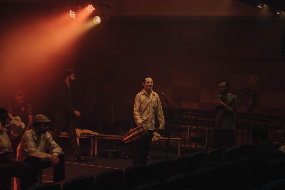Actors in a dimly lit theater rehearsing under warm stage lights.